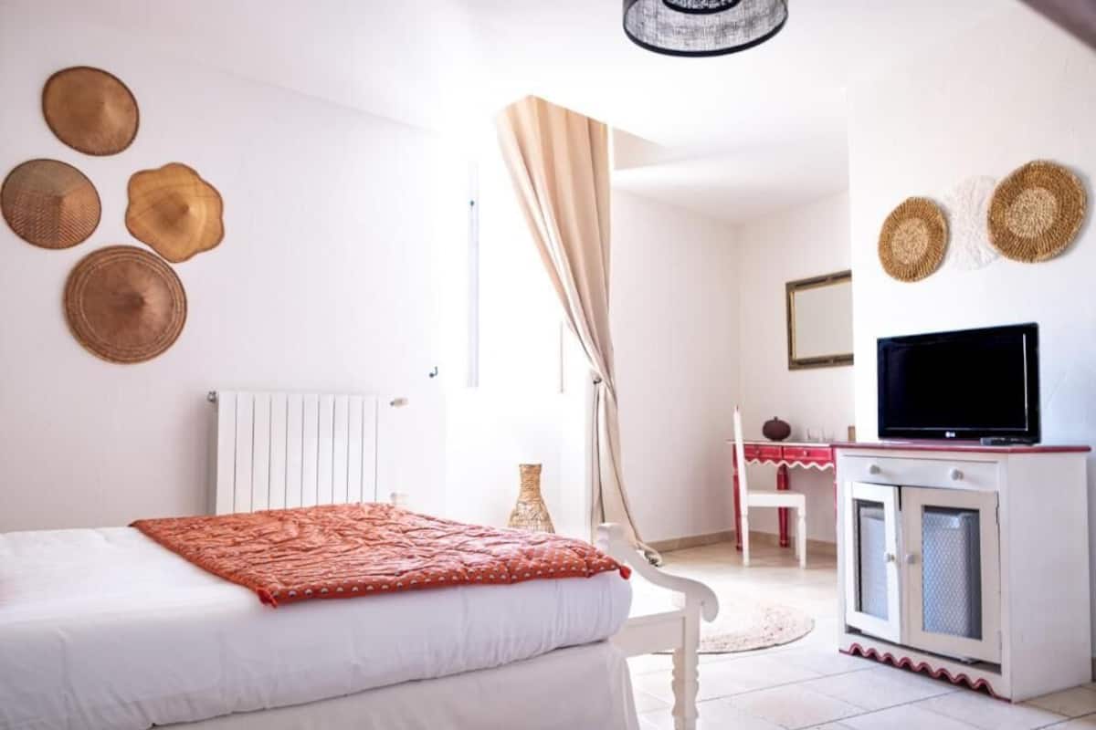 A bedroom with a bed, a television, a desk, and decorative wall hangings.