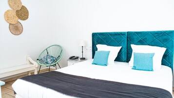 Un lit avec une tête de lit matelassée, une table de chevet avec une lampe, une chaise et un mur orné d’une œuvre d’art tissée.