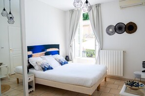 A bedroom with a bed, bedside tables, a window with curtains, a radiator, and wall decor.