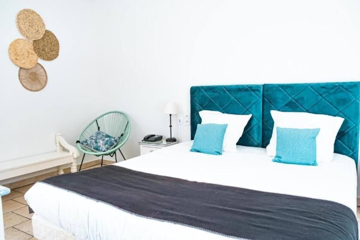 A bed with a quilted headboard, a bedside table with a lamp, a chair, and a wall with woven wall art.