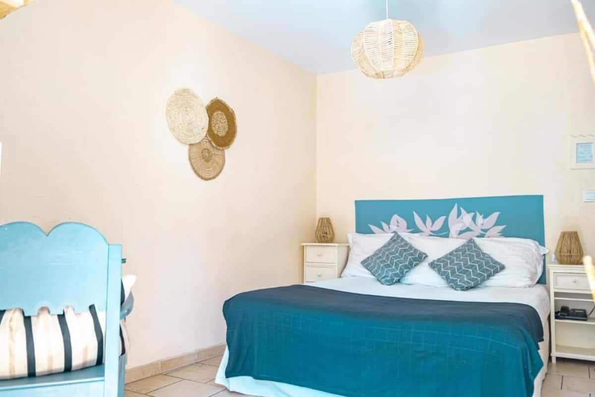 A bedroom with a bed, a chair, a nightstand, and a woven wall hanging.