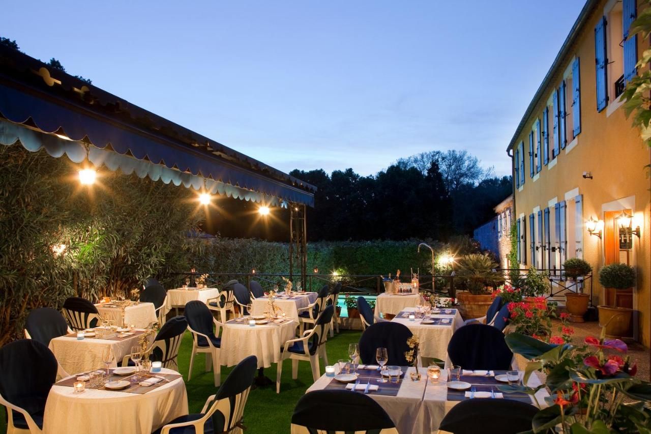 An outdoor dining area with tables set for guests, surrounded by greenery and a building with a balcony.