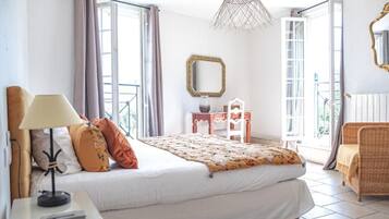Een slaapkamer met een bed, lamp, dressoir, spiegel en stoel.