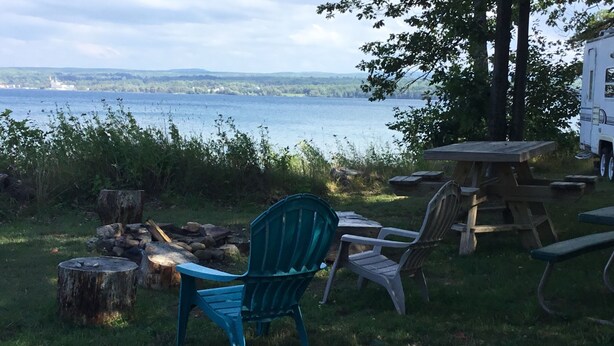 Un terrain de camping au bord du lac, équipé d’un foyer, d’une table et de chaises.