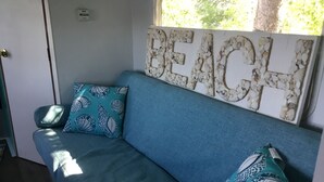 Un canapé bleu agrémenté de coussins à motifs, le mot « PLAGE » écrit sur le mur, et une fenêtre laissant entrer la lumière naturelle.