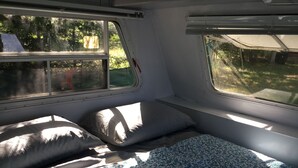 Un intérieur de camping-car compact comprenant un lit, deux fenêtres et un petit banc.