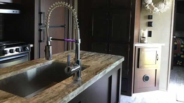 Een keuken met een spoelbak van roestvrij staal, een gasfornuis, donkerhouten kastjes en een decoratieve krans aan de muur.