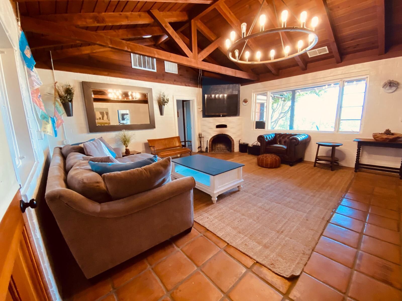 A spacious living room with a large sofa, a coffee table, and a fireplace. There is a television mounted on the wall and a window providing natural light.