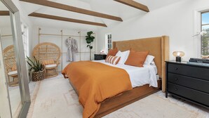 A bedroom with a wooden bed, a nightstand, a dresser, a mirror, and a wicker chair. - Casa Blanca, Secluded Mediterranean Retreat in RSF (Rancho Santa Fe)