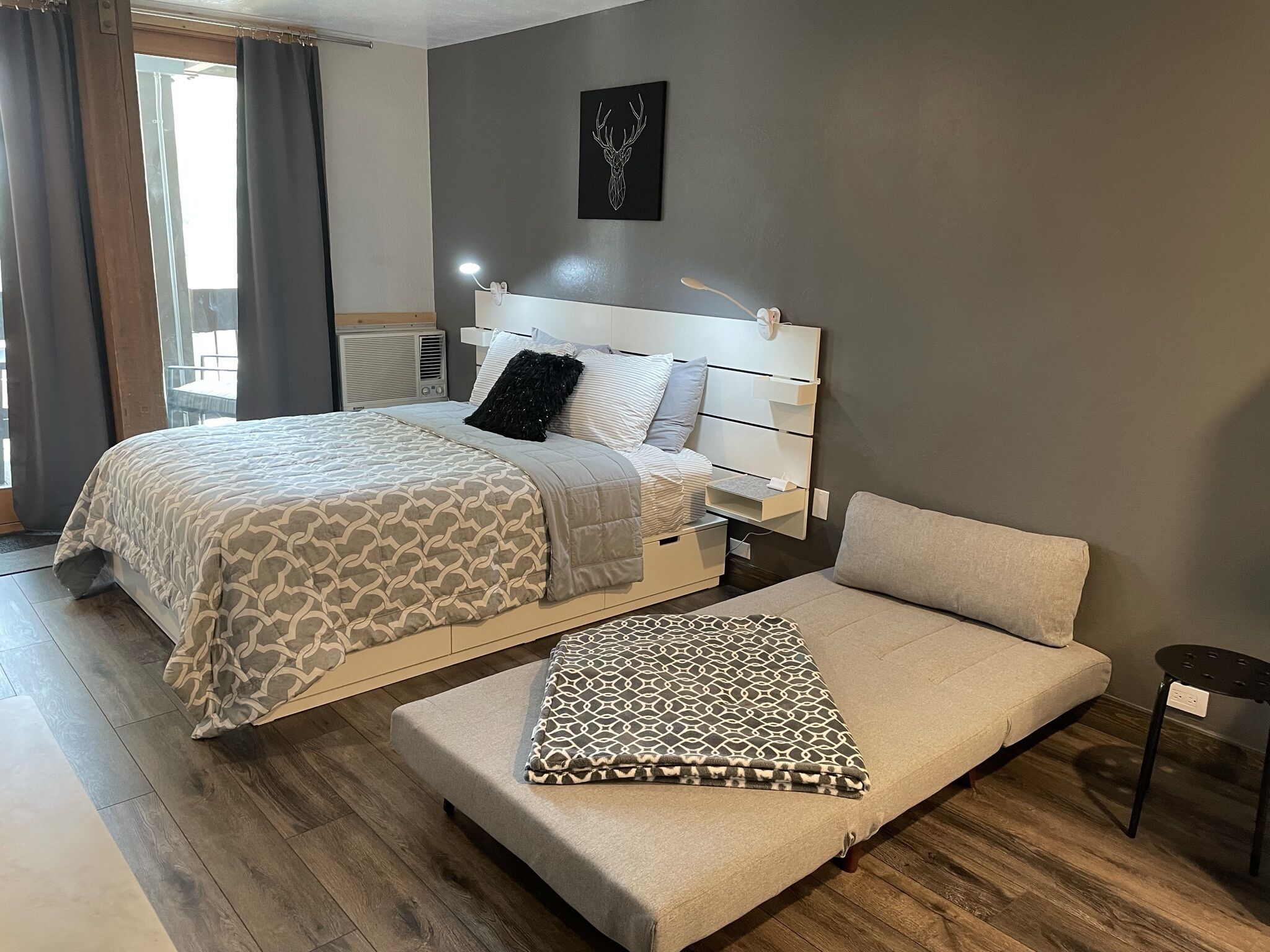 A modern bedroom with a bed, bedside tables, a sofa, and a wall-mounted artwork.