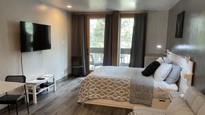 A hotel room with a bed, a desk, a chair, a television, and a balcony with curtains.
