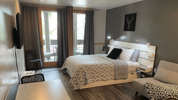 A modern hotel room with a bed, a desk, a chair, and a sofa.