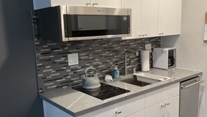 A modern kitchen with white cabinets, a built-in microwave, a kettle, and a coffee maker.