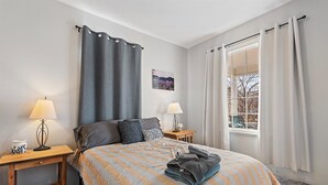 A neatly arranged bedroom with a bed, two bedside tables, a window with curtains, and a wall-mounted picture. - Walking Distance to Town__Discount Ski Passes __TRAVELERS WELCOME (La Grande)