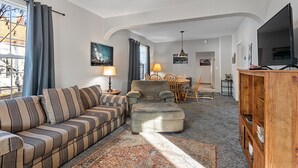 A living room with a sofa, ottoman, and a wooden cabinet. There is a dining area with chairs and a table in the background. - Walking Distance to Town__Discount Ski Passes __TRAVELERS WELCOME (La Grande)