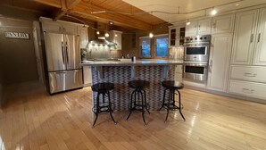 Cocina moderna con vigas de madera, electrodomésticos de acero inoxidable, salpicadero de azulejos y una zona de bar con taburetes.