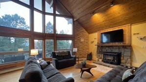 Un salón amplio con ventanas grandes, una chimenea y un televisor de pantalla plana.