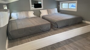 Une chambre avec deux lits, un grand miroir, une fenêtre et un ventilateur de plafond.