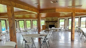Un vaste espace intérieur doté de hauts plafonds et de poutres en bois, aménagé avec de nombreuses tables et chaises, idéal pour les repas ou les réunions.