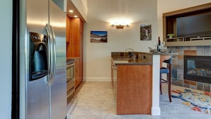 Une cuisine moderne dotée d’un réfrigérateur encastré, de meubles en bois, d’une cheminée en pierre et d’un petit îlot central avec un évier.