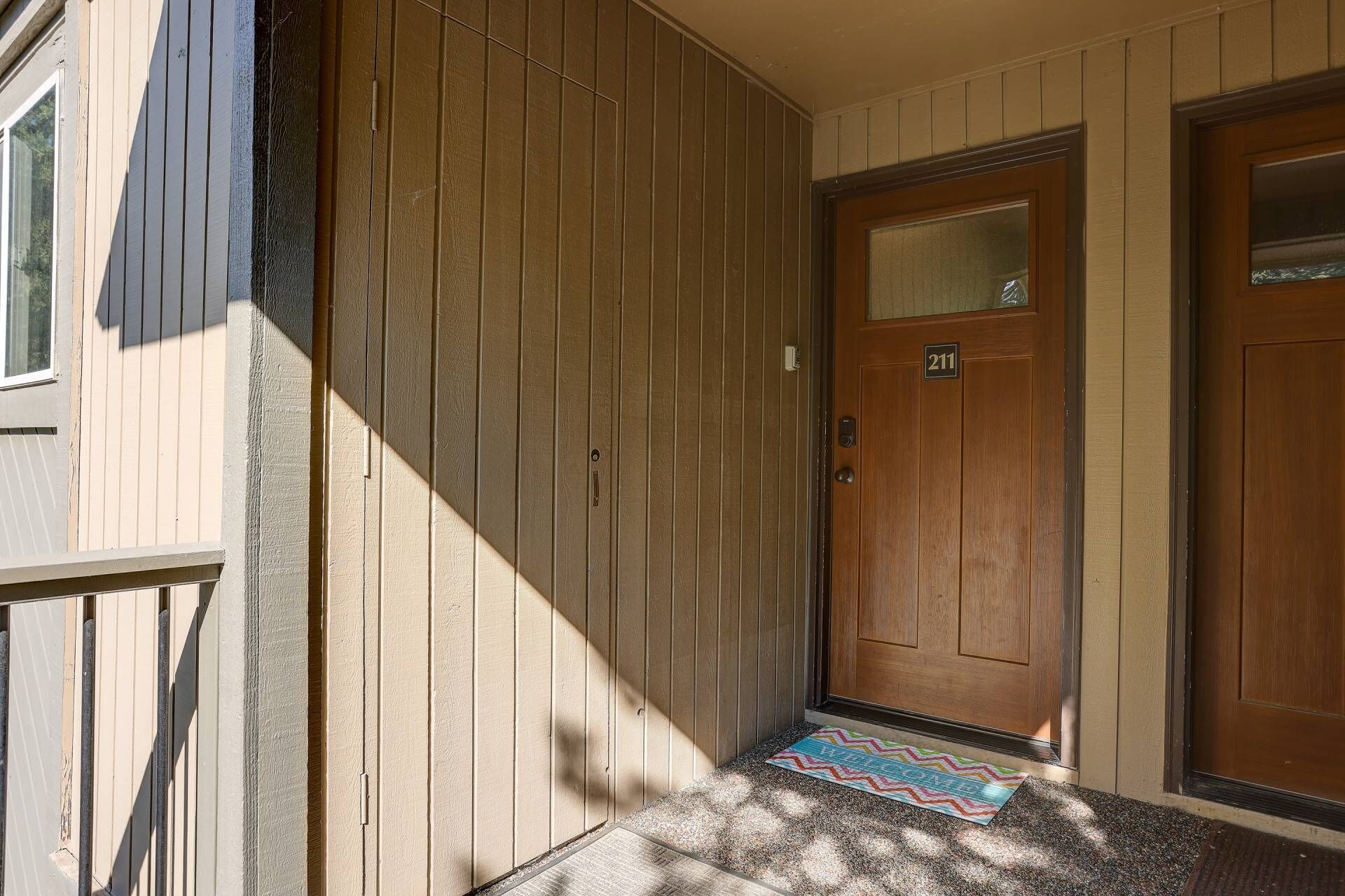A wooden door with a number plate, a small window, and a colorful rug on a textured mat.