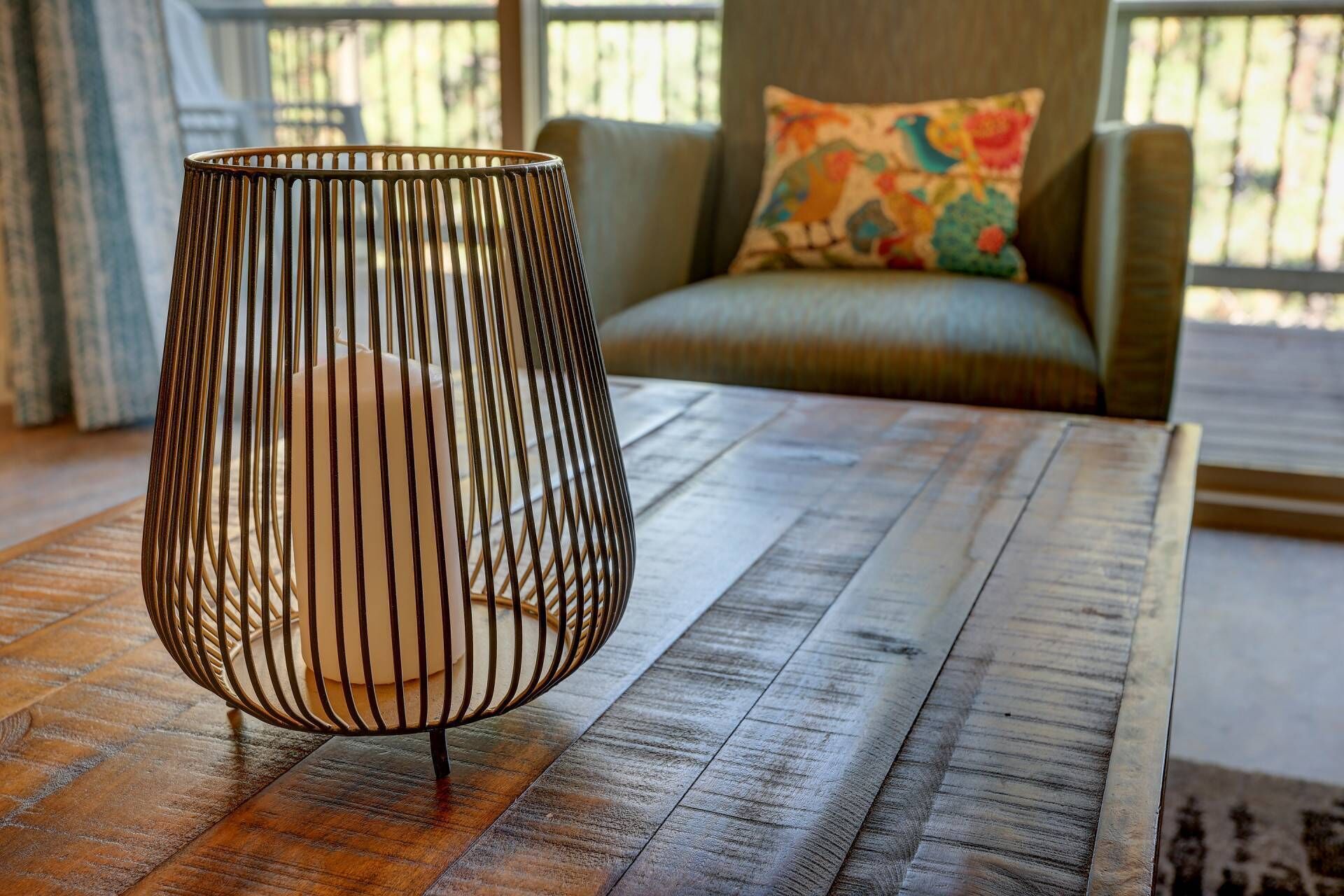 Une pièce avec une table en bois, une lampe en métal et un canapé agrémenté d’un coussin coloré.