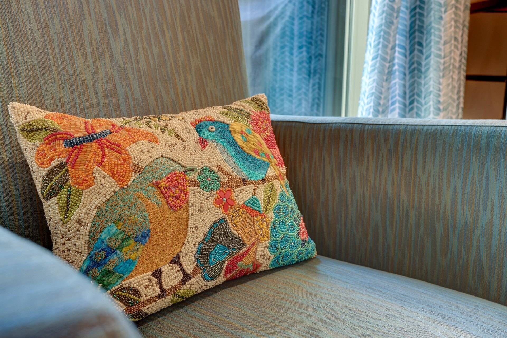 A chair with a colorful beaded pillow featuring a bird design.