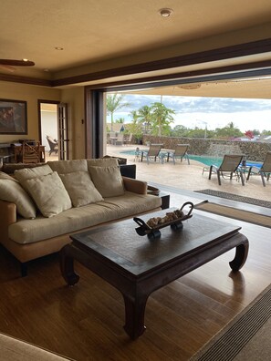 A living room with a sofa, coffee table, and a view of an outdoor pool area. - Mini resort; house with salt water private pool, near the best beaches! (Waikoloa)
