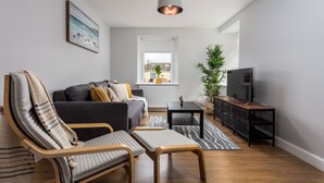A modern living room with a sofa, two chairs, a small table, a television, and a potted plant. - Shore View - Donnini Apartments (Prestwick)