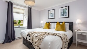 A bedroom with a bed, two bedside tables, a window with curtains, and two framed pictures on the wall. - Shore View - Donnini Apartments (Prestwick)