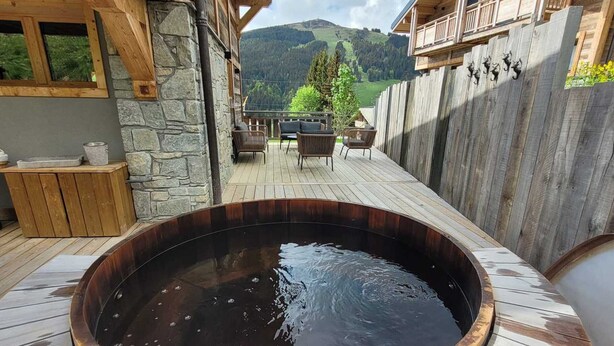 A hot tub on a wooden deck with stone walls, a stone bench, and a view of a mountainous landscape.