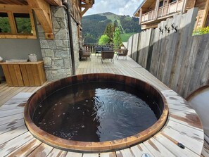 Ein Whirlpool auf einer Holzterrasse mit Steinmauern, einer Steinsitzbank und Blick auf eine Berglandschaft.