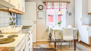 A kitchen with a stove, sink, and cabinets. There is a dining table with chairs and a window with curtains. - Gorgeous home in Markaryd (Markaryd)