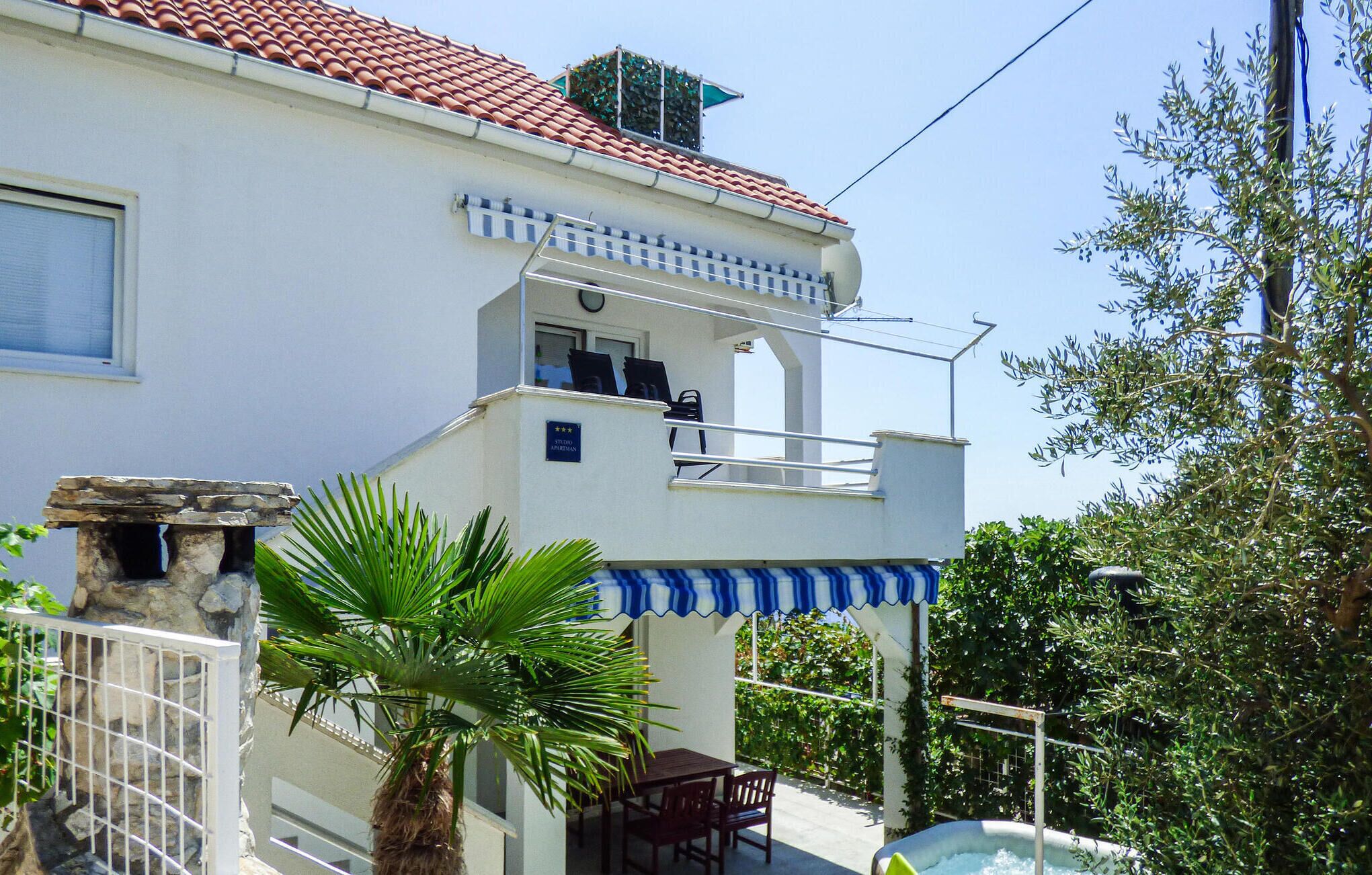 A two-story building with a red-tiled roof, a balcony with outdoor seating, and a pool area.