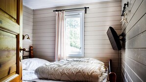 Une chambre à coucher avec un lit, une fenêtre avec des rideaux, un téléviseur fixé au mur et une porte.