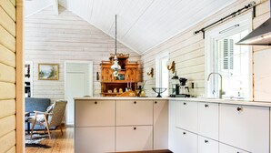 Une cuisine avec des meubles de rangement en bois, un luminaire suspendu et une fenêtre avec des stores.