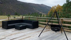Une terrasse dotée d’un canapé d’angle noir, d’un pot suspendu noir et d’une rambarde en bois offrant une vue sur un paysage montagneux.