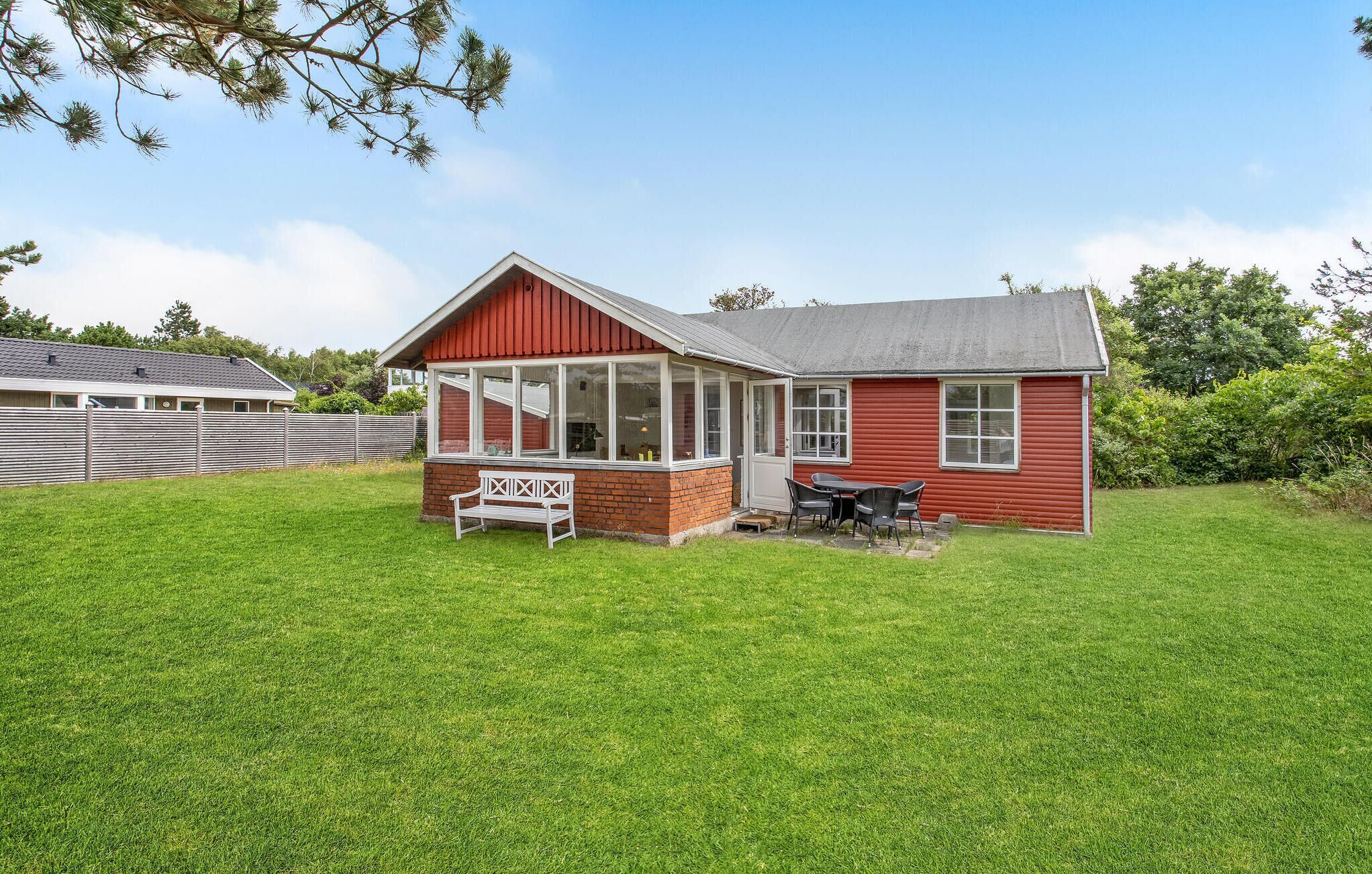 Ett rött hus med en inglasad veranda och en gräsmatta.