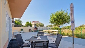 Une terrasse extérieure avec une table et des chaises, un barbecue et une vue sur un arbre et un bâtiment en arrière-plan.