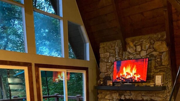A cozy living room with a stone fireplace, leather sofa, and a television. - HOT TUB,  Unique A-Frame Cabin, Walk to ski resort (Mars Hill)