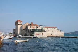 A historic stone building with a tower, located by a calm body of water with several boats docked nearby. - Sunflower-beautiful Modern Apt. w. Terrace&garden (Kastela)