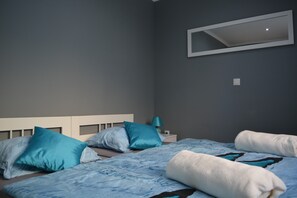 Un dormitorio con cama, almohadas, mesita de noche, lámpara y espejo en la pared.