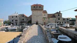 Un chemin de pierre mène à un bâtiment historique doté d’une tour, qui est entouré d’eau et de bateaux.
