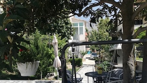 Un espace extérieur aménagé en patio, avec une table et des chaises, entouré de plantes en pot et d’arbres.