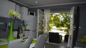 Une cuisine moderne avec des meubles blancs, un coin repas avec une table et des chaises vertes, et une porte-fenêtre coulissante donnant sur un espace de détente extérieur.