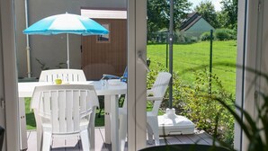 Un patio con tavolo e sedie, un ombrellone e vista su un prato verde e una casa sullo sfondo.