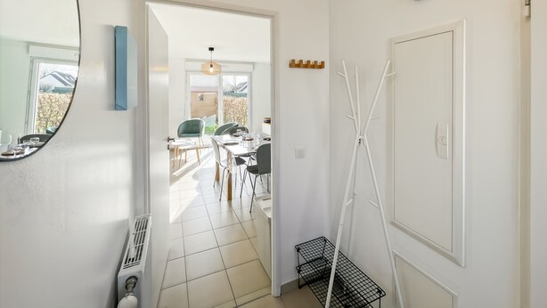 Un corridoio con uno specchio, un termosifone, una porta e un muro bianco.