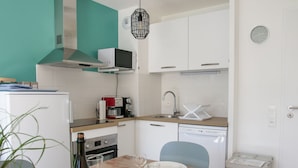 Una cucina funzionale con forno a microonde, macchina del caffè e lavastoviglie. C'è un tavolo da pranzo apparecchiato con piatti e bicchieri, e una bottiglia di vino.