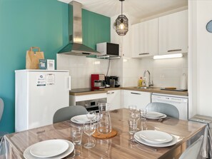 A modern kitchen with white cabinets, a stainless steel range, a red coffee maker, and a dining table set with plates and glasses.