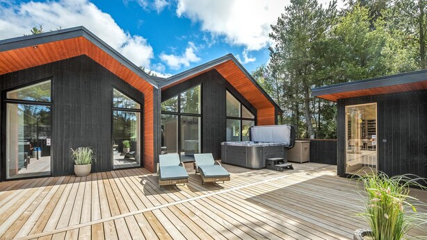 A modern outdoor deck with wooden flooring, lounge chairs, and a hot tub. - Lovely home in Blåvand with sauna (Blåvand)
